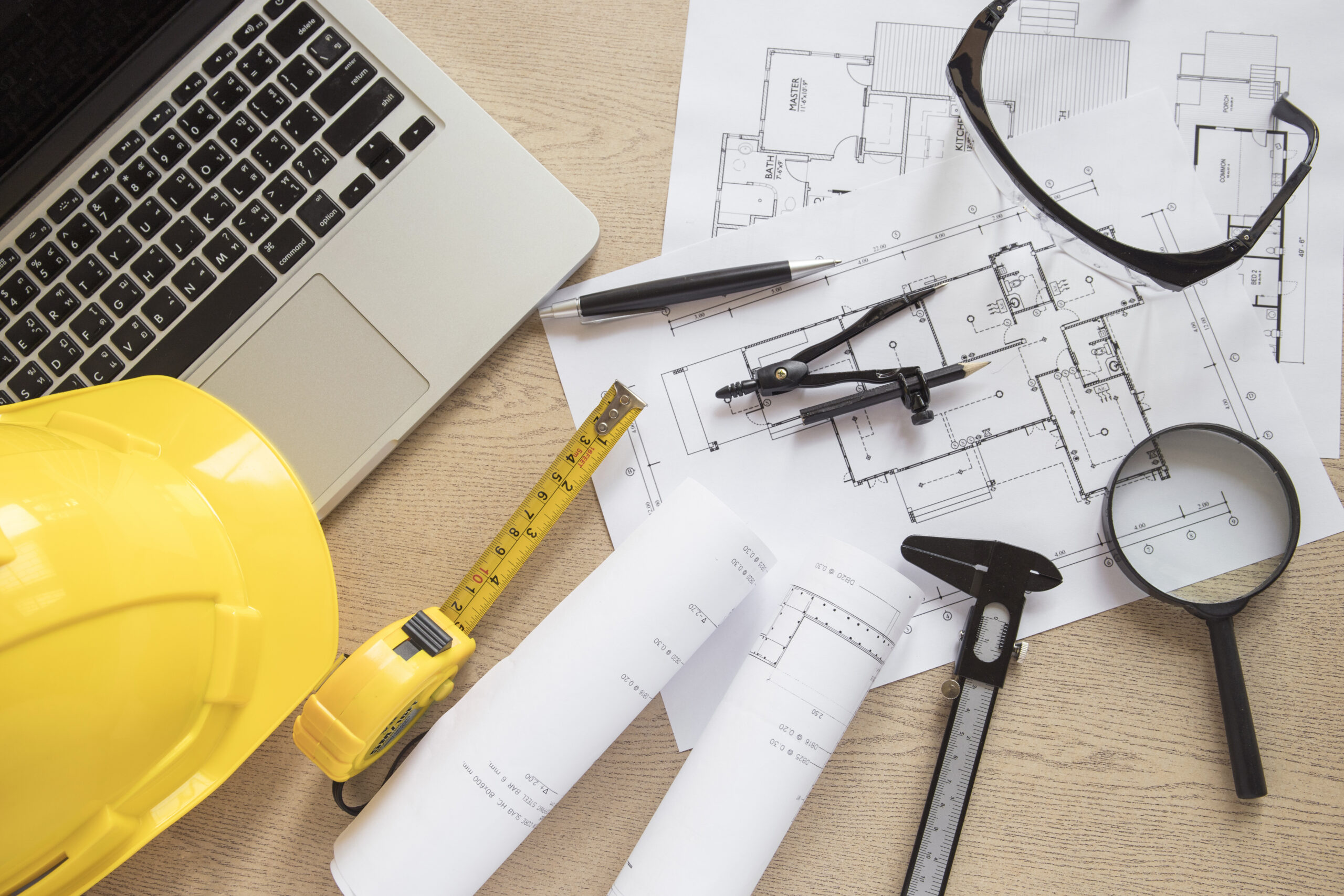 Plano de ingeniería civil sobre mesa con portátil y herramientas de delineación